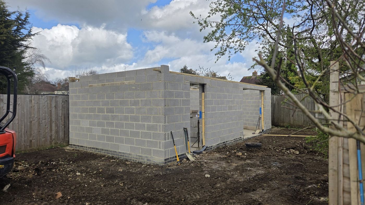 Blockwork shell going up. Walls built off a brick plinth, with door openings formed.